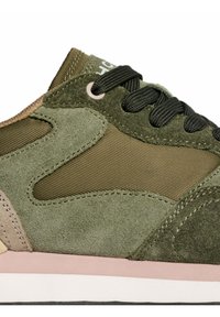 Close-up of olive green suede and fabric sneaker with black laces and light pink midsole details.