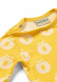 Tutina di cotone gialla con una ripetuta fantasia bianca di frutta, dotata di scollatura rotonda e bottoni a pressione per una vestizione facile.