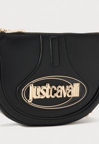 Borsa a tracolla in pelle nera con logo ovale in tono oro, texture liscia e chiusura con zip e dettagli di cucitura pronunciati.