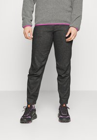 Hiilenharmaat jogger-housut, joissa on kapeutettu leikkaus ja hienovarainen tekstuuri. Yhdistetty mustiin lenkkareihin, joissa on violetteja ja oransseja yksityiskohtia.