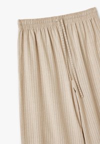 Pantaloni beige leggeri con un motivo a righe verticali bianche. Presentano una vita elastica e un cordoncino per una vestibilità regolabile.