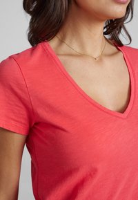 T-shirt a collo v-v in cotone morbido, con maniche corte e una texture liscia. Presenta cuciture minime lungo il colletto.
