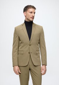 Lichtbruine blazer met een slim fit, twee knopen en een notch lapel, gecombineerd met een zwarte turtleneck eronder.
