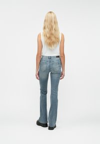 Jeans acampanados para mujer en denim azul claro, con cintura de altura media, diseño de cinco bolsillos y detalles de costuras visibles. Zapatos gruesos negros.