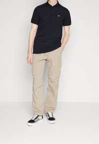 Černé polo triko s malým logem, spárované s béžovými cargo kalhotami s bočními kapsami a černými teniskami s bílou podrážkou.