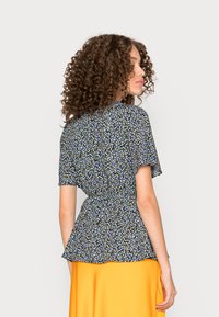 Blusa peplum floral em azul-escuro com padrões brancos e amarelos, mangas curtas e um laço na cintura; combinada com uma saia laranja brilhante.
