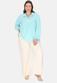 Himmelblaue Bluse mit langen Ärmeln und Kragen, strukturierter Stoff, geraffte Taille, kombiniert mit cremefarbenen, weit geschnittenen Hosen und beigen Ballerinas.