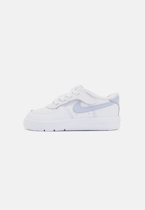 Balti Nike Air Force 1 sportbačiai su lygiu odiniu viršumi, perforuotais pirštais ir šviesiai mėlynu akcentu ant kulno.