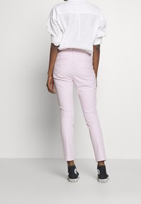 Pantalon en vichy rose à coupe slim, fabriqué en tissu léger. Associé à une chemise blanche et des baskets montantes noires.