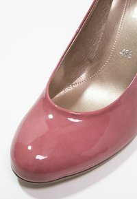 Chaussure à talon haut en cuir verni rose avec un bout rond et une finition brillante. L'intérieur est en matériau synthétique beige clair doux. Taille 41/2.