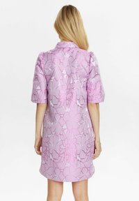 Rochie cu mânecă scurtă, de culoare roz deschis, cu un model floral în roz închis. Dispune de un guler și are o croială lejeră, cu lungime până la genunchi.
