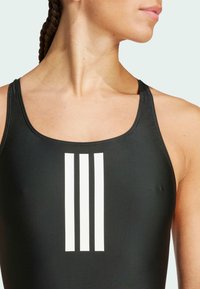 Crni sportski kupaći kostim s glatkom teksturom, s tri horizontalne bijele pruge sprijeda. Jednostavan, klasičan dizajn s širokim trakama.