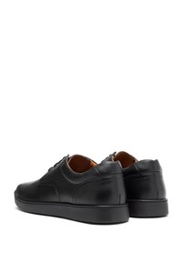 Scarpe in pelle nera con finitura testurizzata, punta rotonda, design a profilo basso e suola in gomma nera liscia. Cuciture sulla parte posteriore.