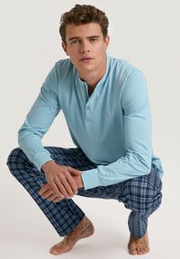 Lichtblauw langemouwen top met een henley-nek en twee knopen, gecombineerd met donkerblauwe geruite pyjamabroek met rode en witte accenten.