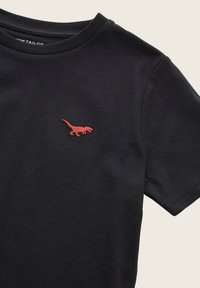 T-shirt in cotone nero con un piccolo dinosauro ricamato in rosso all'area sinistra del petto; maniche corte e scollatura rotonda.