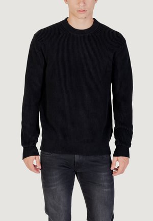 Maglione nero a coste con colletto rotondo, caratterizzato da maniche lunghe e una finitura testurizzata. Abbinato a jeans grigio scuro, con uno stile minimalista.