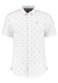 Camisa de manga corta blanca con pequeños patrones geométricos rojos y azules, cuello abotonado y una etiqueta en el lado izquierdo cerca del dobladillo.