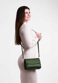 Zelená kožená kabelka přes rameno s klopou, zlatými detaily a nastavitelným popruhem, vystavená na čistém bílém pozadí.