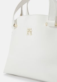 White leather handbag with gold hardware accents and a prominent logo. Structured shape with top handles and stitching details.