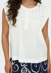 Haut en lin blanc à manches courtes, avec des plis verticaux et une patte de boutonnage, conçu pour une coupe ample.