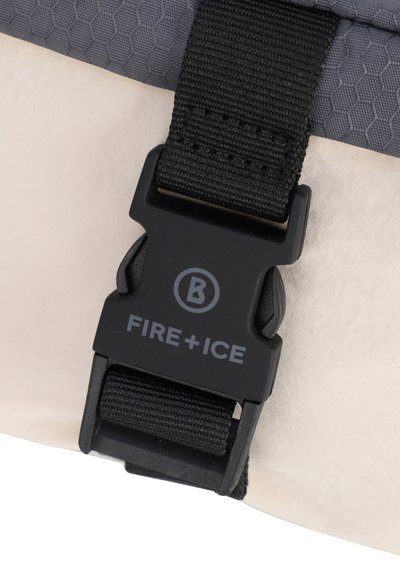Fibbia in plastica nera con logo "FIRE+ICE" su tessuto grigio testurizzato, attaccata a un materiale beige liscio. Presenta una cinghia di regolazione.