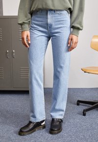 Light blue denim jeans with a straight leg fit, high waist, and subtle fading, paired with black shoes featuring a buckle detail.