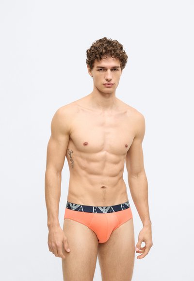 Cuecas masculinas laranja com uma faixa elástica azul-marinho na cintura que tem um logótipo. O tecido parece suave e justo, com um design clássico de cueca.