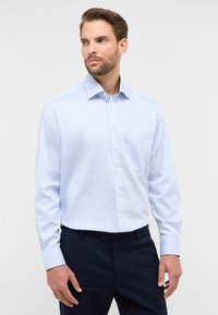 Camicia a righe blu chiaro con colletto, apertura con bottoni e taschino sul petto. Tessuto morbido con maniche lunghe.