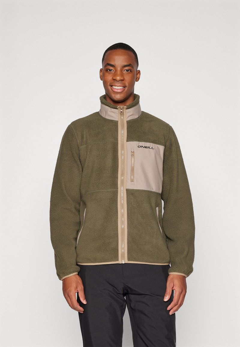 Chaqueta de forro polar verde oliva con un panel frontal en color beige claro y cierre con cremallera, que presenta un cuello alto y un logo en el pecho. Tejido texturizado.