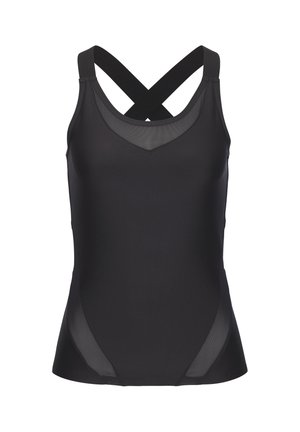 Fit woman in black athletic wear stands with hand on hip in a bright, sandy outdoor setting under clear blue sky.
