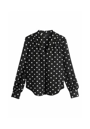 Mustast kangast pluus valgete täppidega, V-kaelusega, pikkade volangvarrukatega ja kõverdatud äärega. Valmistatud siledast materjalist.