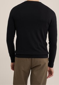 Svart stickad tröja med långa ärmar, rund hals och ribbade muddar och fåll. Bärs över ljusbruna byxor. Slät textur.