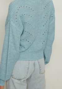 Light blue knitted sweater featuring a loose fit, long sleeves, and a textured pattern with small cutouts along the back.