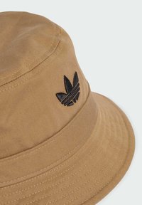 Cappello a secchiello in tela marrone con logo ricamato nero, dotato di una larga visiera e tessuto testurizzato per una maggiore durata.
