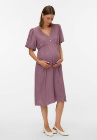 Nėštumo suknelė melsvai violetine spalva, su v-kaklu, trumpomis pūstomis rankovėmis ir mygtukų detale krūtinėje. Pagaminta iš lengvos, struktūruotos medžiagos.