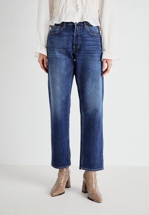 Jeans in denim blu ad altezza vita, dritti e con una texture scolorita. Abbinati a stivaletti beige lucidi con punta square e tacco a blocco.