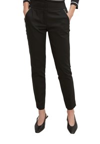 Zwarte taps toelopende broek met een gladde textuur, voorzien van ritszakken en een op maat gemaakte pasvorm, eindigend bij de enkel. Draagstukken met zwarte ballerina's.