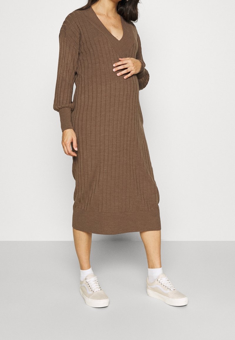 Robe tricotée marron mi-longue avec un décolleté en V et une texture côtelée. Présente des manches longues et une coupe décontractée, associée à des baskets légères.