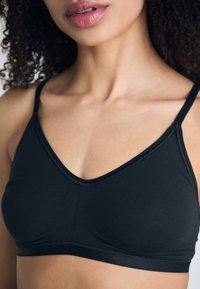 Soutien-gorge noir avec un design en V, fabriqué à partir d'un tissu lisse. Il dispose de bretelles réglables et d'une construction sans coutures pour un confort optimal.