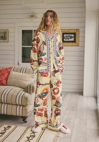 Set de haine de casă din material galben cu modele maritime multicolore. Include o cămașă cu nasturi și pantaloni cu picioare largi, asortați cu papuci albi.