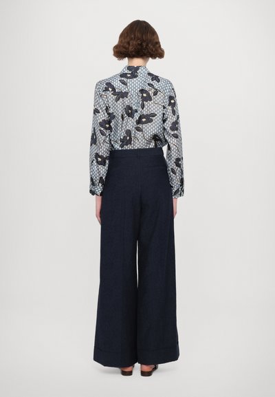 Blau gemustertes Hemd mit dunkler Hose. Das Hemd hat florale Designs und geometrische Formen. Die Hose ist weit geschnitten mit einem umgeschlagenen Saum.