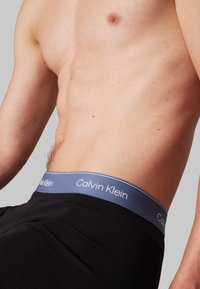 Fekete pamut boxer alsónadrág kék elasztikus derékpánttal, fehér "Calvin Klein" felirattal. Simb textúra, testhezálló kialakítás.