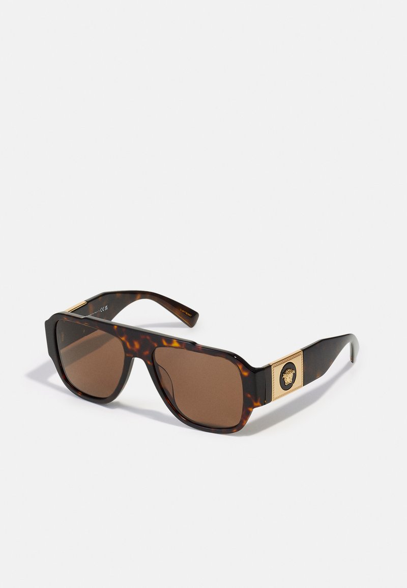 Ochelari de soare cu carapace țestoasă, cu lentile maronii, formă rectangulară largă și accesorii de nuanță aurie, având un medalion decorativ pe dita.
