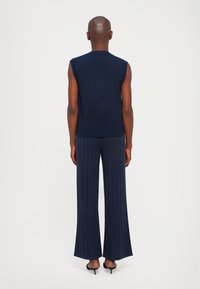 Marineblå ermeløs strikket topp kombinert med matchende vide ribbede bukser. Jevn tekstur, tettsittende design og subtil ribbestruktur på stoffet.