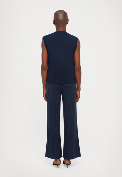 Marineblå ermeløs strikket topp kombinert med matchende vide ribbede bukser. Jevn tekstur, tettsittende design og subtil ribbestruktur på stoffet.