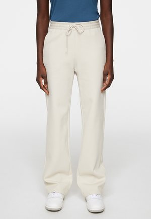 Beige wijdvallende sweatpants met een elastische tailleband en trekkoord. Gecombineerd met witte sneakers lijkt de stof zacht en glad.