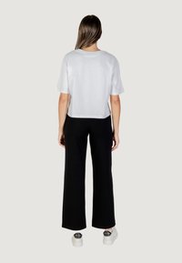 Witte cropped t-shirt met korte mouwen, gecombineerd met zwarte wijde broek. Gekenmerkt door witte sneakers met zilveren accenten.
