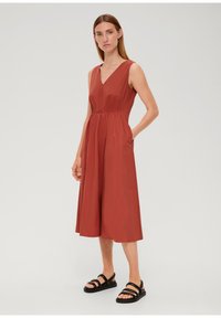 Roestkleurige mouwloze jurk met een V-hals, een cinched taille en zijzakken, met een vloeiende, knie-lange rok.