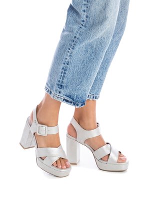 Sandales à talons hauts argentées métalliques avec des brides croisées et une boucle à la cheville. Talon bloc épais et design à bout ouvert. Texture lisse.