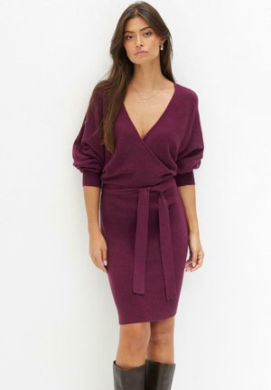 Robe enveloppante en maille bourgogne avec un décolleté en V profond, des manches bouffantes et une taille cintrée. Texture lisse, design à mi-genoux avec une silhouette ajustée.